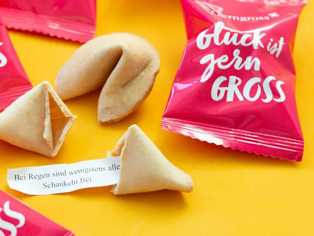 Gebrandete Glückskekse mit Botschaft „Glück ist gern GROSS“ auf farbigem Hintergrund: detailreiches Grafikdesign und aufmerksamkeitsstarke Werbung, entwickelt in der Kreativagentur Wien von einer Werbeagentur aus Wien.